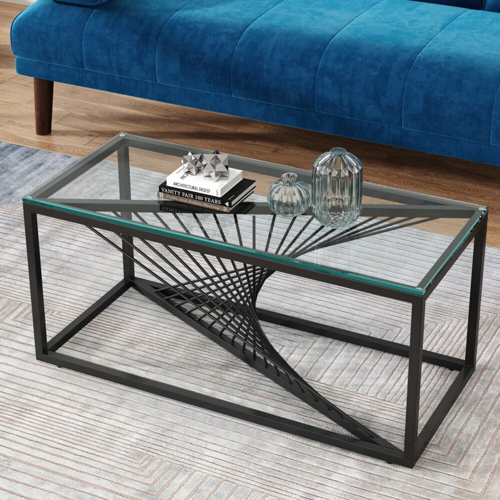 Rectangular glass-top coffee table with black metal starburst base, angled view with blue sofa, potted plant and decorative
