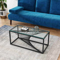 Rectangular glass-top coffee table with black metal starburst base, angled view with blue sofa, potted plant and decorative