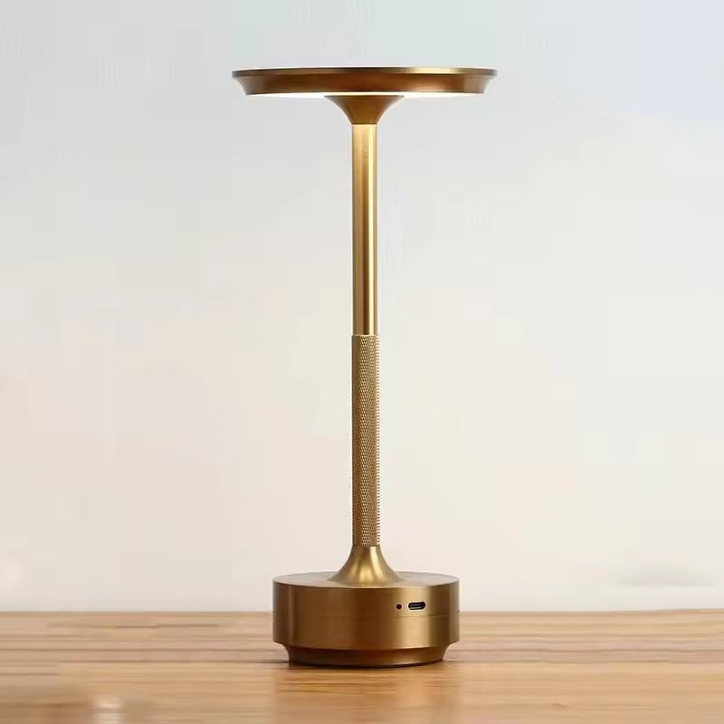 Gold slim-stem table lamp with flat disc shade on wooden surface, knurled stem and USB-C port on circular base