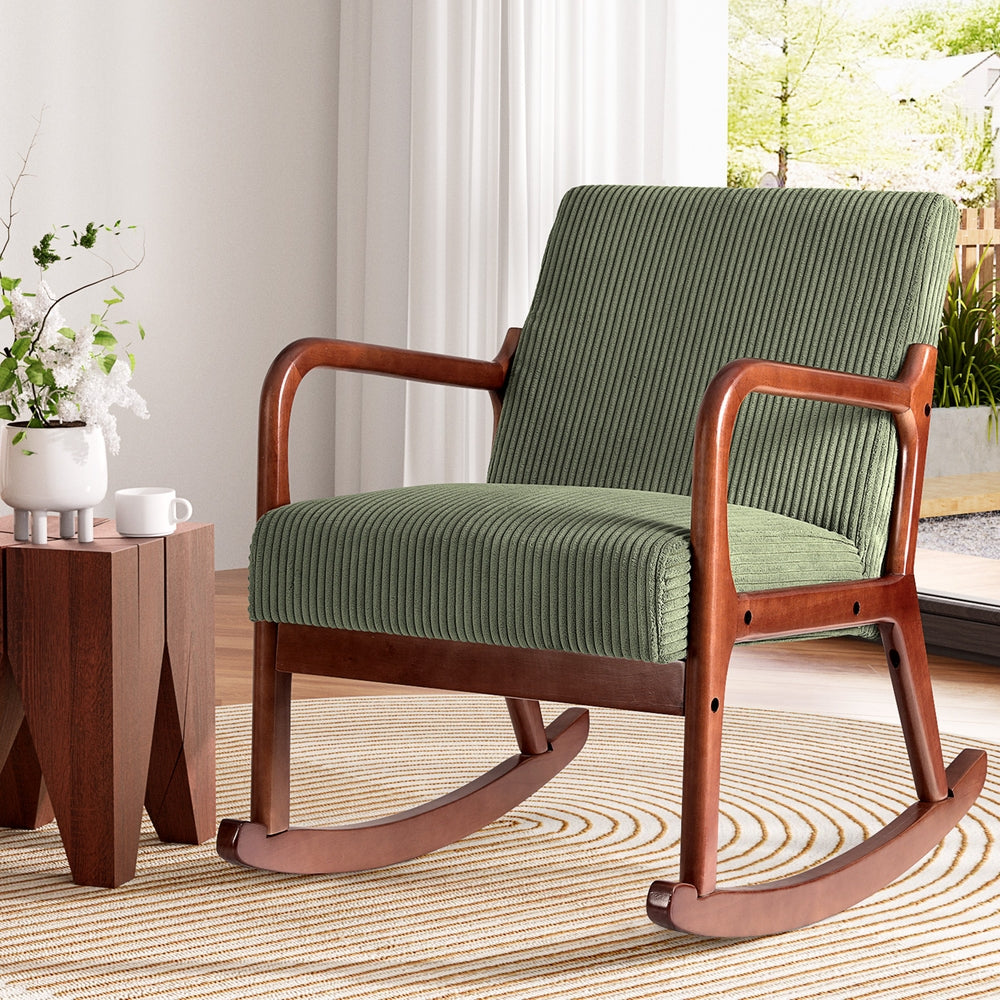 Green corduroy rocking chair with dark wood frame on circular rug in bright room, side table with plant vase beside