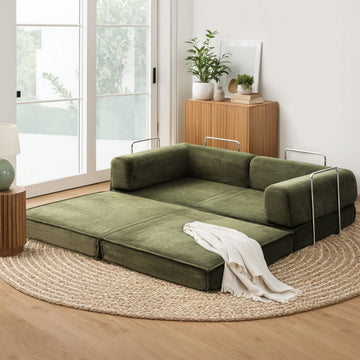 Green corduroy folding sofa bed fully extended on jute rug in living room; chrome arm handles and white throw blanket
