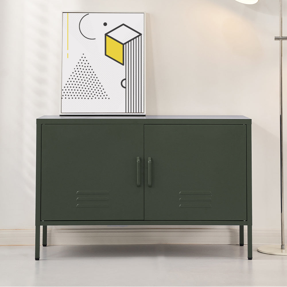 Dark green metal two-door locker cabinet with vent slots on thin legs in living room setting with geometric art print on top