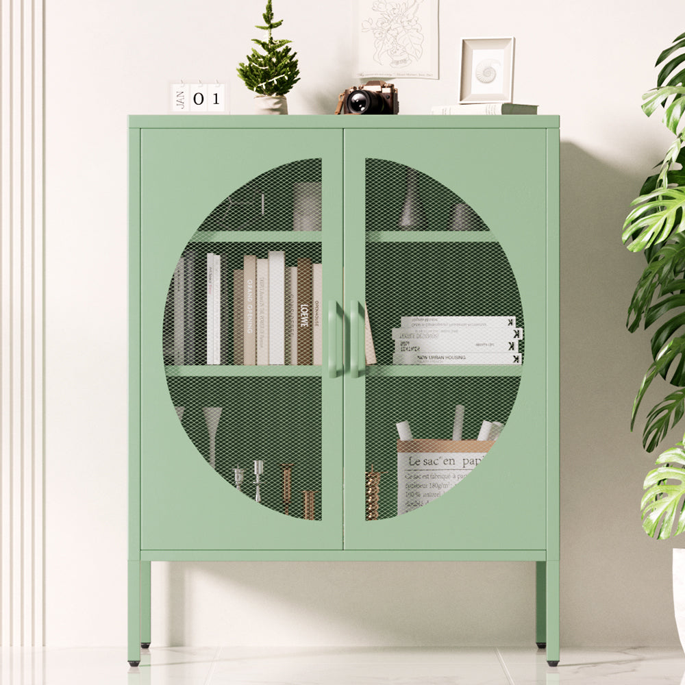 Sage green two-door metal sideboard with circular mesh door panels, books and decor inside, in room setting