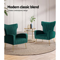 Two dark green velvet wingback armchairs with gold legs and gold side table on jute rug, 