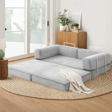 Grey corduroy folding sofa bed fully extended on jute rug in living room; chrome arm handles and white throw blanket