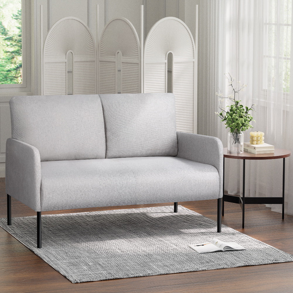 Light grey fabric 2-seater sofa with black metal legs in room, arched room divider and round side table with vase