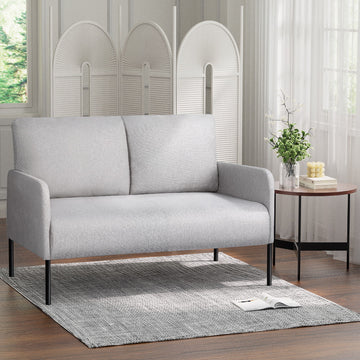 Light grey fabric 2-seater sofa with black metal legs in room, arched room divider and round side table with vase