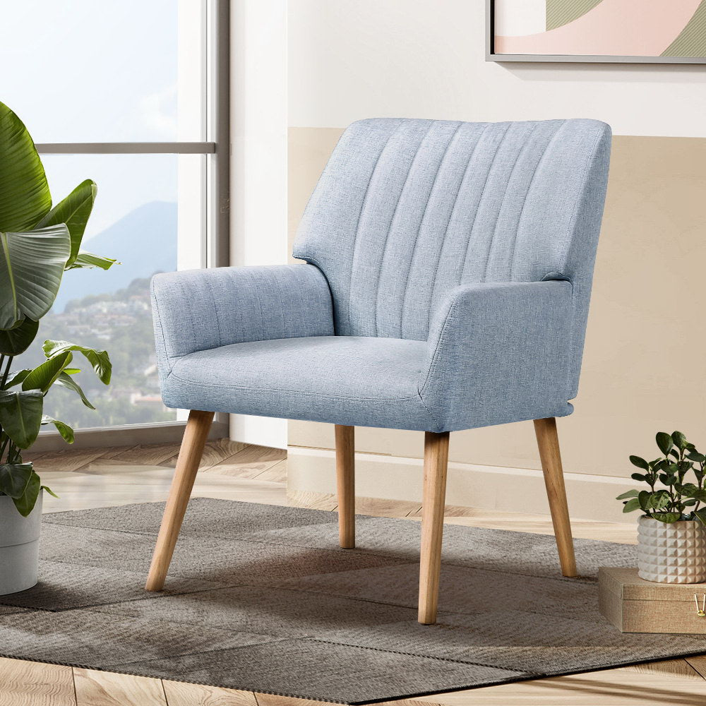 Light grey fabric accent chair with vertical channel stitching in lifestyle room setting with large tropical plant