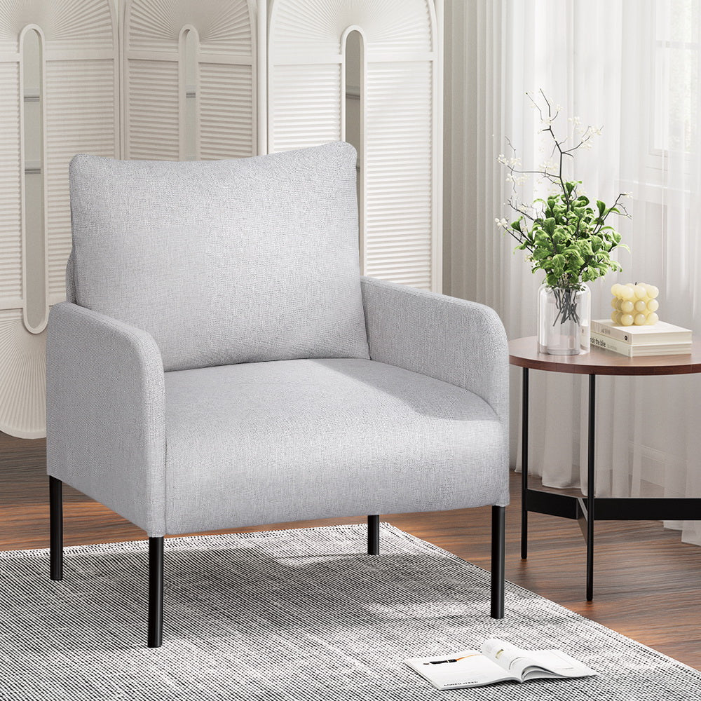 Light grey fabric armchair with black metal legs in living room with folding screen, side table with flowers and magazine
