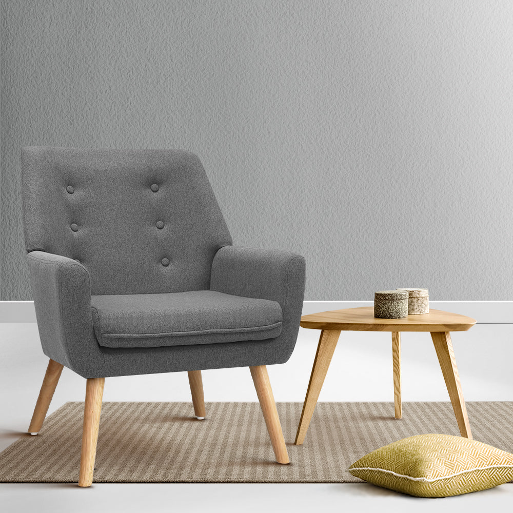 Grey fabric button-tufted armchair with wood legs on striped rug, round wood side table and yellow floor cushion in grey room