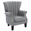 Grey fabric wingback armchair with gold nailhead trim on arms, black legs, side-angle view on white background