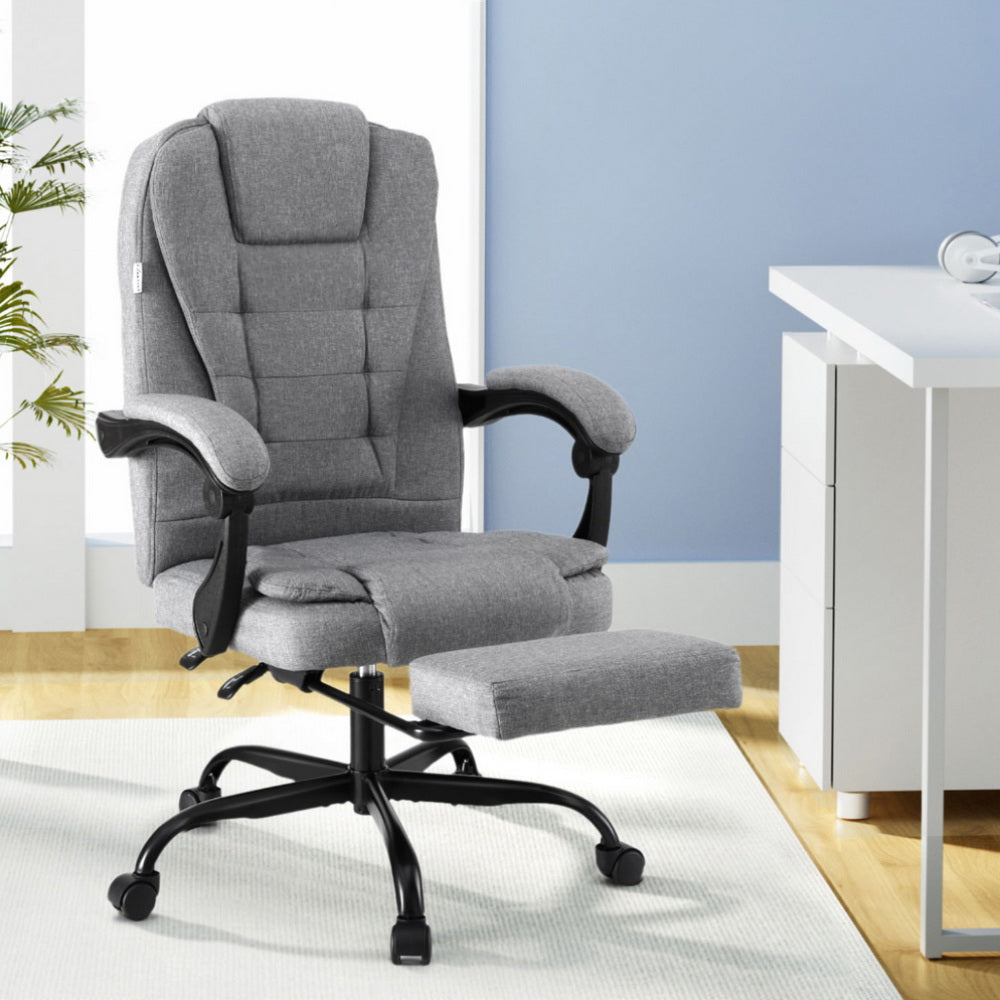 Grey fabric high-back office chair with footrest extended in lifestyle home office setting near white desk