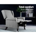 Grey fabric wingback recliner with footrest extended in lifestyle scene, reclines 100 to 135 degrees, Total comfort text