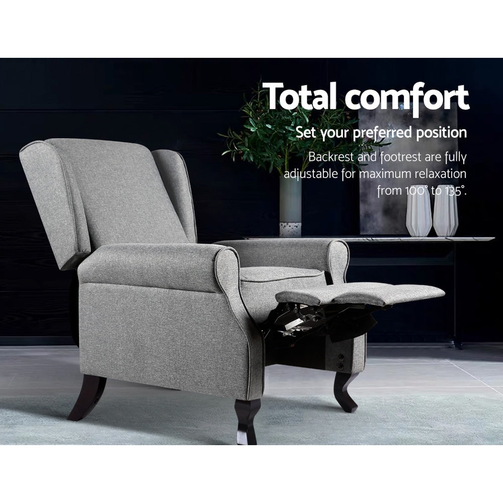 Grey fabric wingback recliner with footrest extended in lifestyle scene, reclines 100 to 135 degrees, Total comfort text