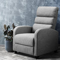Grey fabric recliner chair with segmented padded back beside rubber plant, grey concrete textured wall and herringbone floor