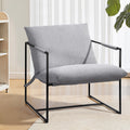 Grey fabric sling armchair in room with sheer curtains and light wood floor, bookcase at left, large plant at right
