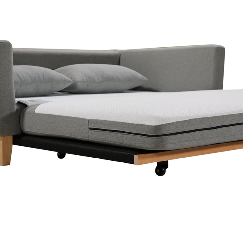 Close-up of grey fabric sofa bed partially extended showing white mattress foot and black casters on wood base