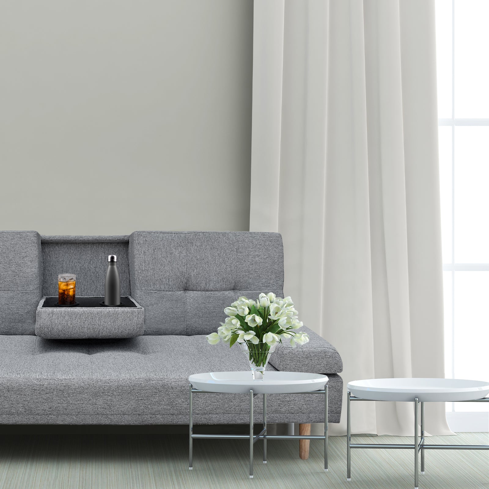 Grey fabric sofa bed with fold-down cup holder tray open holding drinks and water bottle in living room