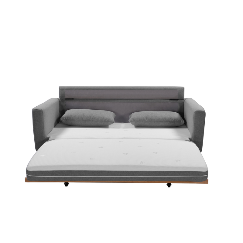 Grey fabric sofa bed fully extended showing white mattress, two scatter pillows and wood frame base with casters