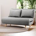 Grey fabric 2-seater sofa bed in lifestyle living room setting on round rug with indoor plants