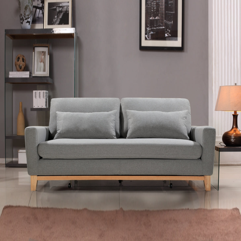 Grey fabric sofa bed fully extended showing white mattress, two scatter pillows and wood frame base with casters