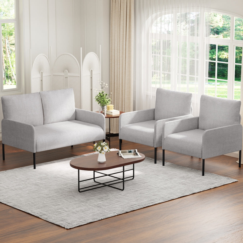 Grey fabric armchair and two-seater loveseat set in bright room with arched window, oval coffee table and flowers