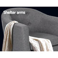 Grey fabric tub armchair close-up showing button-tufted back and shelter arms with cream throw draped, Shelter arms text