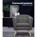 Grey fabric tub armchair with button-tufted back and wood legs in dark lifestyle room with Enamoured presence text