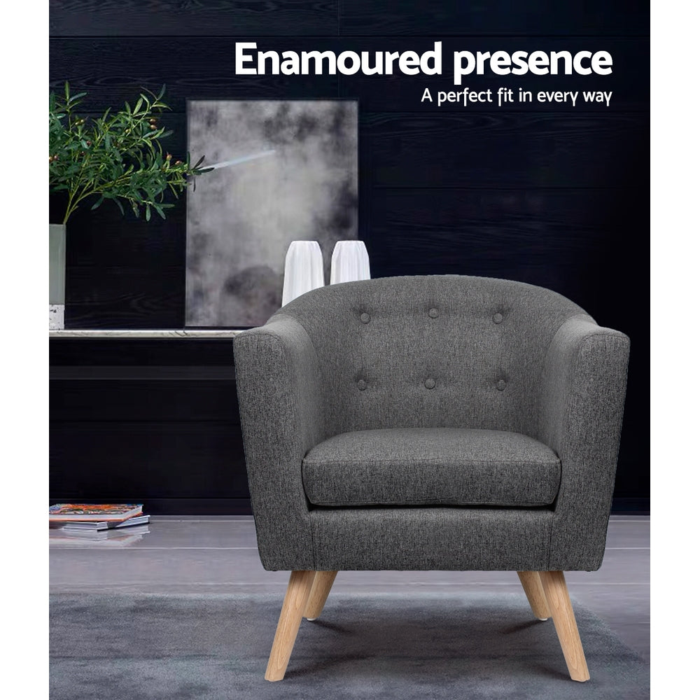 Grey fabric tub armchair with button-tufted back and wood legs in dark lifestyle room with Enamoured presence text