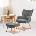 Grey fabric button-tufted wingback armchair and ottoman, natural wood legs, lifestyle room with wooden desk and open book
