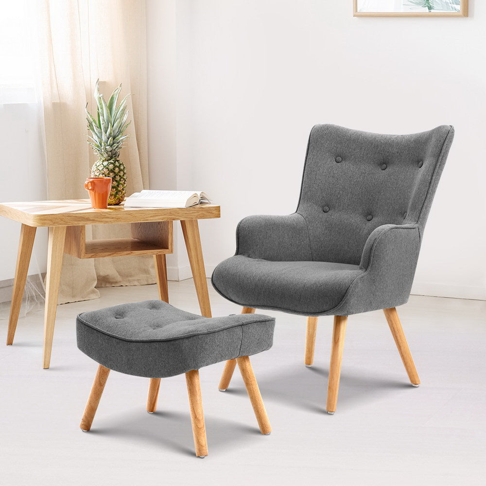 Grey fabric button-tufted wingback armchair and ottoman, natural wood legs, lifestyle room with wooden desk and open book