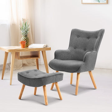 Grey fabric button-tufted wingback armchair and ottoman, natural wood legs, lifestyle room with wooden desk and open book