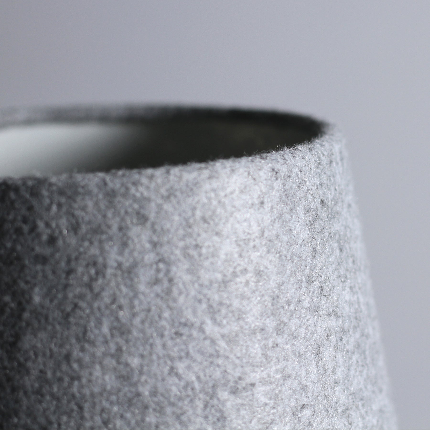 Close-up of top of light grey felt lamp shade showing dark interior and tapered textured exterior