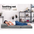Woman lying on grey linen floor lounger flat in room with metal shelf unit and decorative plants