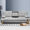 Grey linen sofa bed with cupholder tray holding two coffee cups on striped rug, side table with teapot