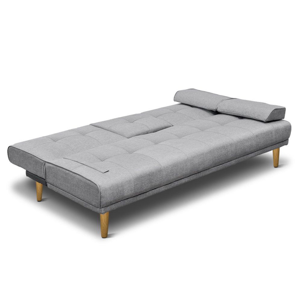Grey linen sofa bed fully reclined flat on white background with two bolster pillows at head end and wood legs