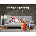 Grey linen sofa bed with polka dot cushions and striped rainbow throw on striped rug against dark textured wall