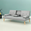 Grey linen sofa bed with open cupholder and two cups against teal wall, yellow vase and black side table