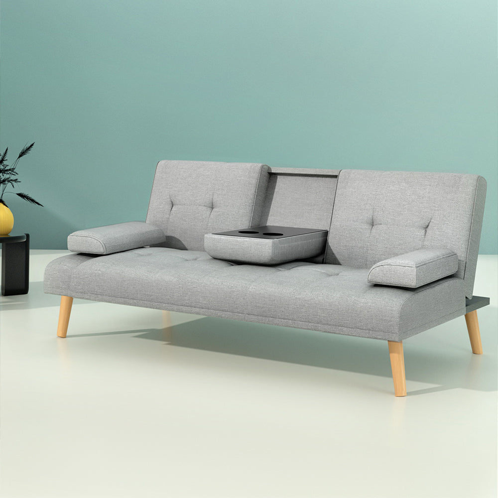 Grey linen sofa bed with open cupholder and two cups against teal wall, yellow vase and black side table