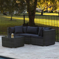 Grey rattan outdoor lounge set with dark cushions and glass coffee table on stone patio beside pool, autumn trees behind