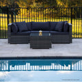 Grey rattan outdoor lounge set with navy cushions beside pool, stone patio, black fence and autumn trees in background