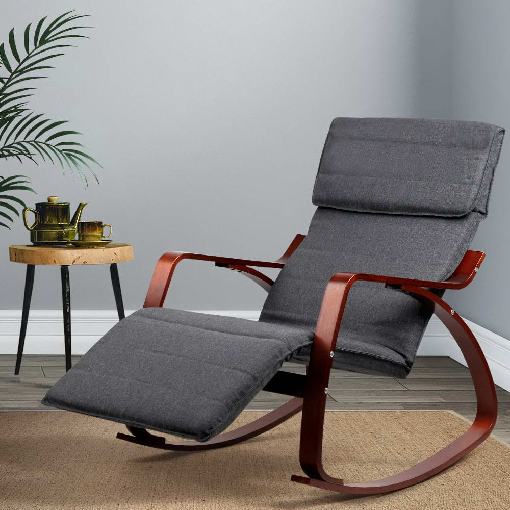 Dark grey fabric rocking recliner with walnut-finish bentwood frame and extended footrest, lifestyle room with palm plant