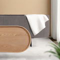 Grey ribbed oval ottoman with natural wood oval lid leaned against side and white throw draped over top