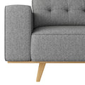 Close-up of grey tufted sofa armrest showing fabric texture, tufted backrest join and natural wood leg