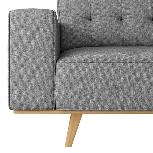 Close-up of grey tufted sofa armrest showing fabric texture, tufted backrest join and natural wood leg