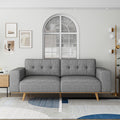 Grey tufted 3-seater sofa front view with natural wood legs in bright white living room with arch window