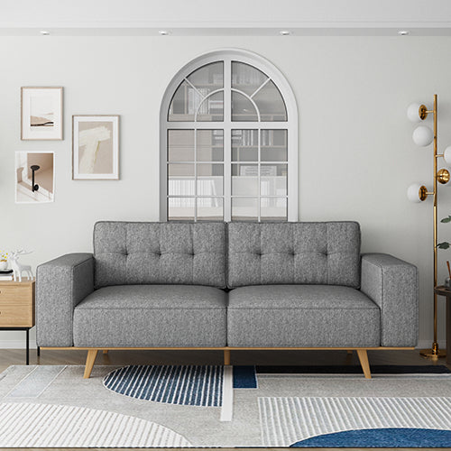 Grey tufted 3-seater sofa front view with natural wood legs in bright white living room with arch window