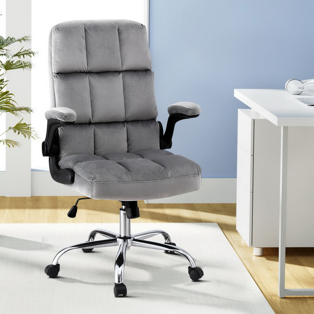 Grey tufted velvet office chair with flip-up armrests and chrome base in modern office with plant and white desk