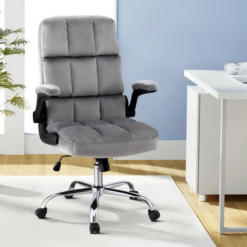 Grey tufted velvet office chair with flip-up armrests and chrome base in modern office with plant and white desk