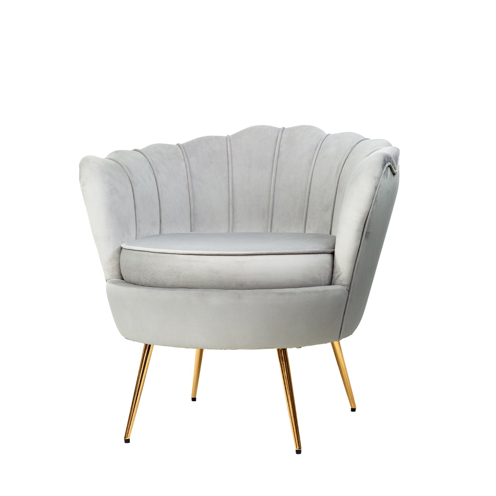 Light grey velvet scallop shell armchair with gold legs beside black side table with gold lamp against light blue wall